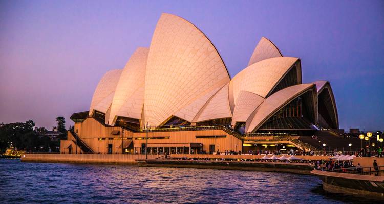 Sydney Opera House lit at dusk with soft pink sky and harbor waters in the foreground.