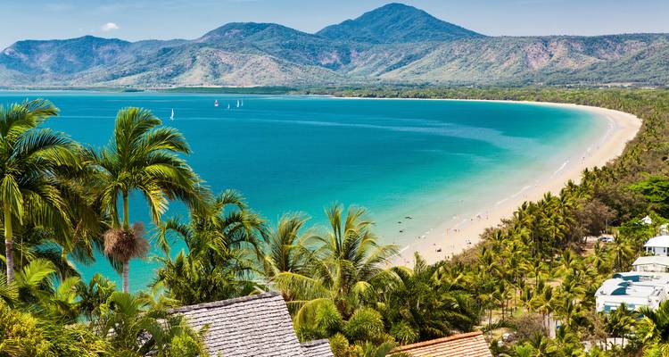 Turquoise bay fringed by coconut palms and backed by forested mountains under blue skies.
