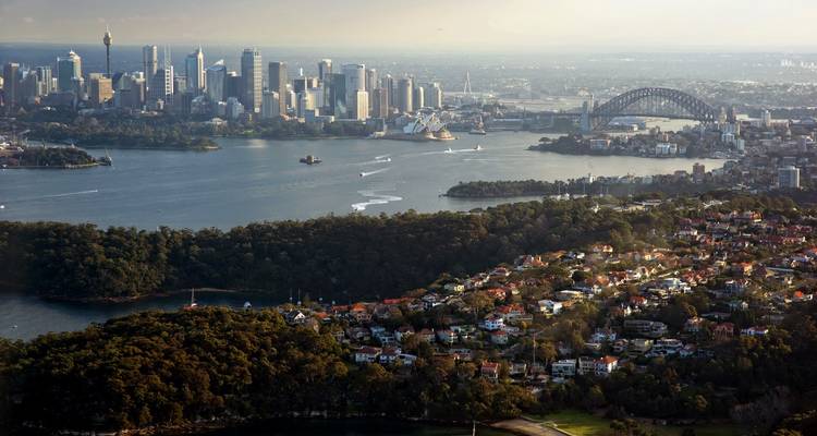 Aerial panorama of Sydney Harbour with skyline, Opera House and Harbour Bridge surrounded by coves and greenery.