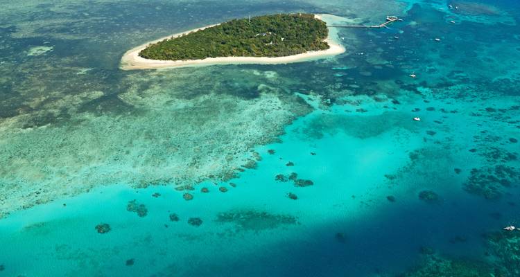 Aerial view of a small green island surrounded by turquoise water and coral reefs in the Great Barrier Reef.