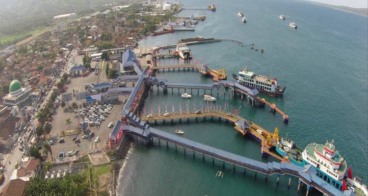 Vista aérea de la terminal de ferry de Gilimanuk con múltiples muelles y barcos en aguas turquesas.
