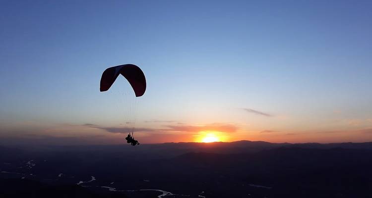Een silhouet van een paraglider die tegen een levendig zonsondergang voorbij kronkelende rivieren en donkere bergkammen omhoog vliegt.
