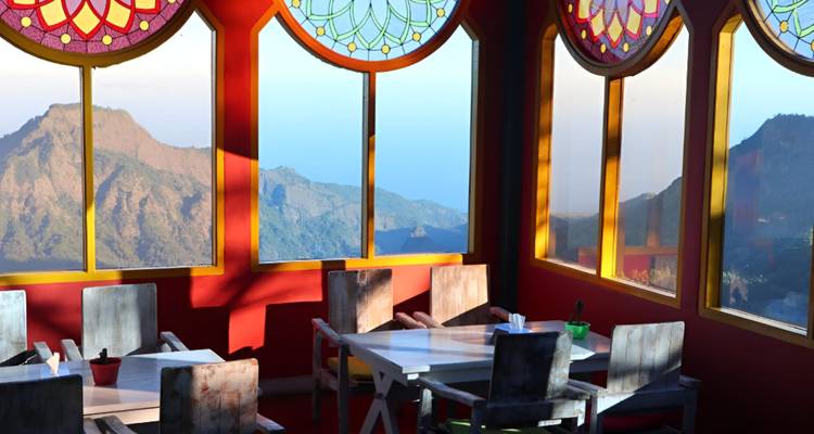Interior del restaurante con vidrieras de colores que dan vista a un hermoso paisaje de montaña.
