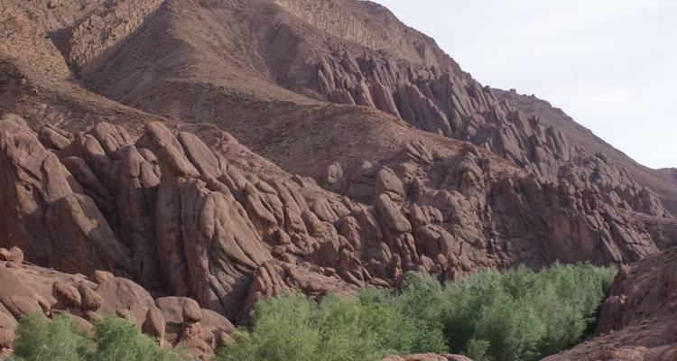 Les formations rocheuses rougeâtres et déchiquetées s'élèvent abruptement au-dessus d'une ligne verte d'arbres dans une vallée sauvage.