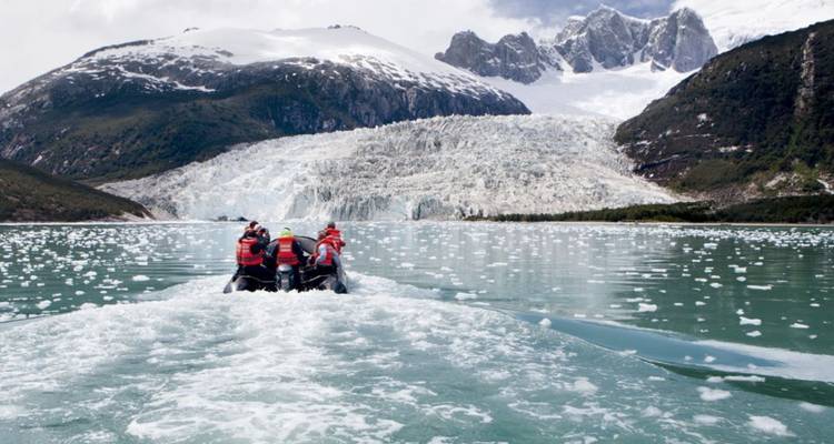 Das Zodiac-Boot von Reisenden nähert sich einer massiven Eiswand eines Gezeitengletschers, der mit Eisbrocken übersät ist.