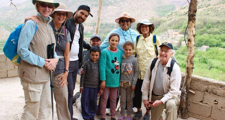 Travellers posing with local children on a terrace overlooking green valleys in the Atlas Mountains.