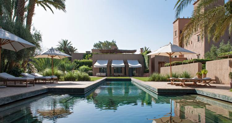 Elegant boutique hotel with pool, sun loungers and palm trees under clear sky.