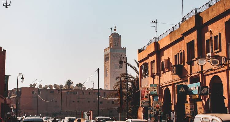 Street scene with Koutoubia minaret rising above ochre buildings and traffic.