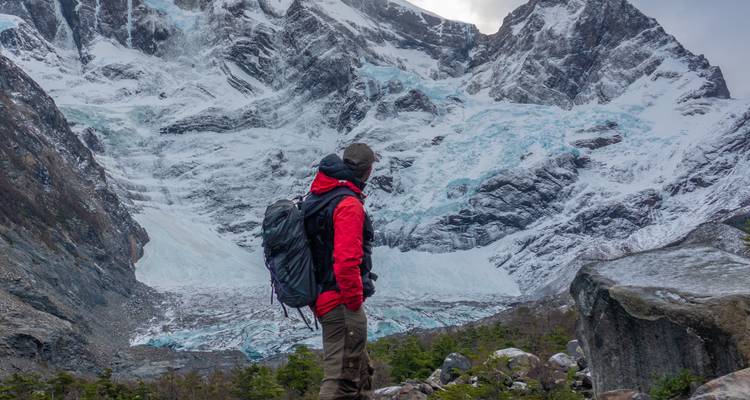 Wanderer in roter Jacke blickt auf einen dramatischen, eisbedeckten Berghang und Gletscher