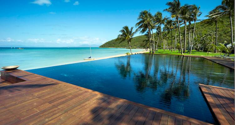 Infinity-Pool spiegelt Palmen und das ruhige türkisfarbene Meer an einem abgelegenen tropischen Strand wider.