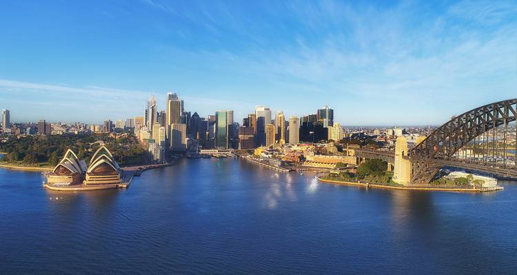 Ikonische Luftaufnahme des Sydneyer Hafens mit dem Opernhaus und der Harbour Bridge unter einem klaren blauen Himmel.