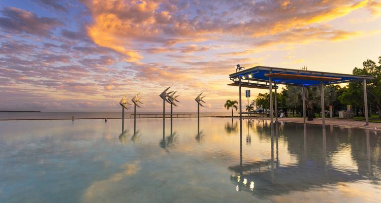 Die Cairns Esplanade Lagoon spiegelt farbenfrohe Sonnenaufgangswolken über dem ruhigen Wasserbecken an der Uferpromenade wider.