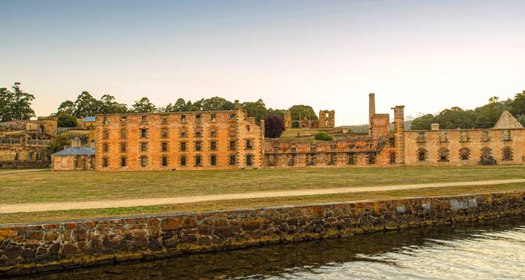 Les bâtiments historiques en grès du pénitencier de Port Arthur se reflétant dans les eaux calmes du port au crépuscule.