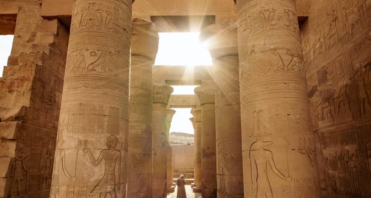 Zonnestralen stromen tussen imposante, met hiëroglieven bedekte zandsteenkolommen in een oud Egyptisch tempel.