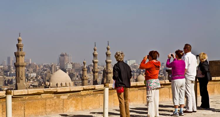 Toeristen maken foto's van Cairo's skyline en minaretten vanaf een stenen terras onder een heldere hemel.