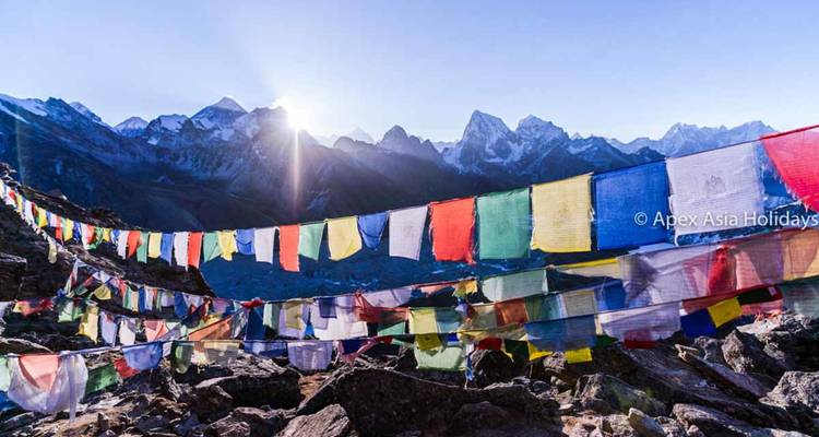 Banderas de oración coloridas ondeando con picos del Himalaya iluminados por la salida del sol.