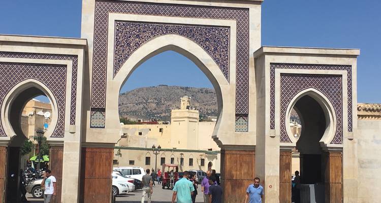 Portail mauresque grandiose présentant un travail de carrelage complexe et de multiples arcs à l'entrée d'une ville, avec des visiteurs qui le traversent.