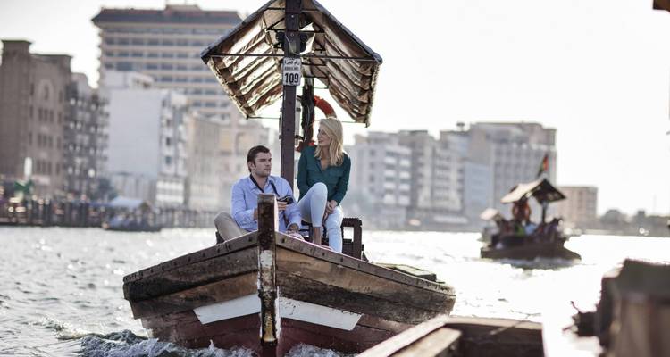 Una pareja disfruta de un paseo tradicional en abra de madera en el Dubai Creek con el horizonte de la ciudad de fondo.