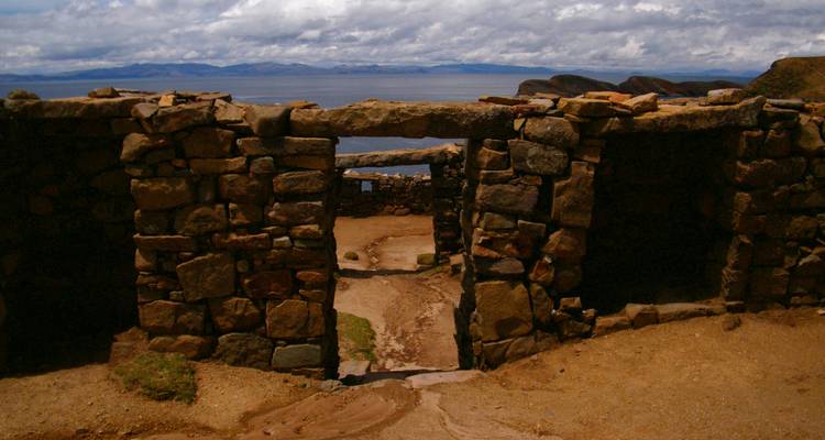 Las ruinas de un portal de piedra se asoman a un enorme lago y montañas distantes bajo un cielo sombrío.