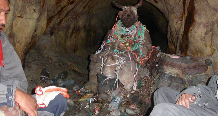 Los mineros se sientan junto a una estatua con cuernos cubierta de serpentinas dentro de un túnel oscuro de una mina en Potosí.