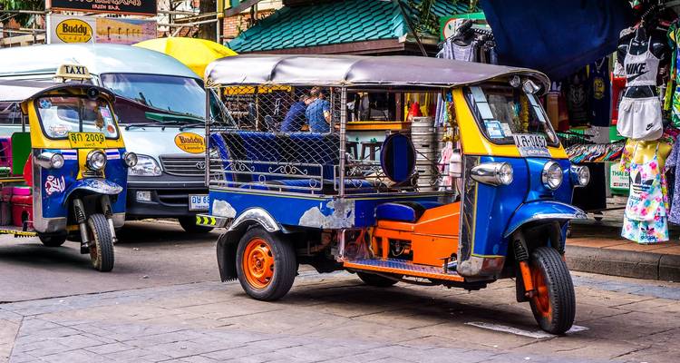 Tuk-tuk de colores brillantes estacionado en un animado mercado callejero de Bangkok con otro taxi detrás.