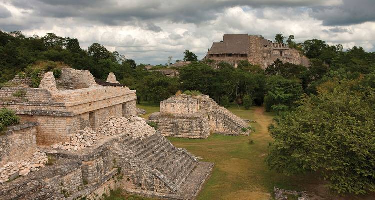 Oude Maya stenen ruïnes verscholen in dichte groene jungle onder een dramatische bewolkte hemel.