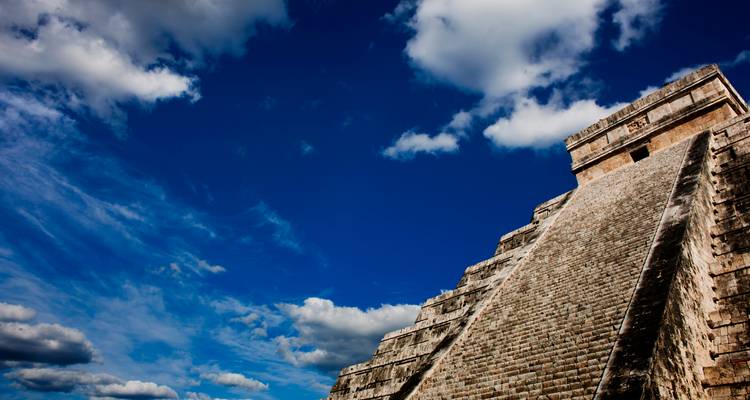De enorme stenen piramide van Chichen Itza rijst steil op tegen een diepblauwe lucht met dramatische witte wolken.