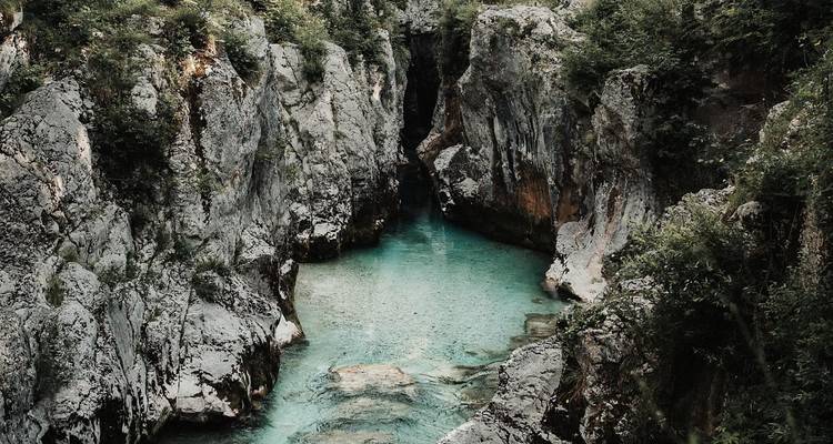 A narrow turquoise river winds through a steep limestone gorge covered with lush greenery.