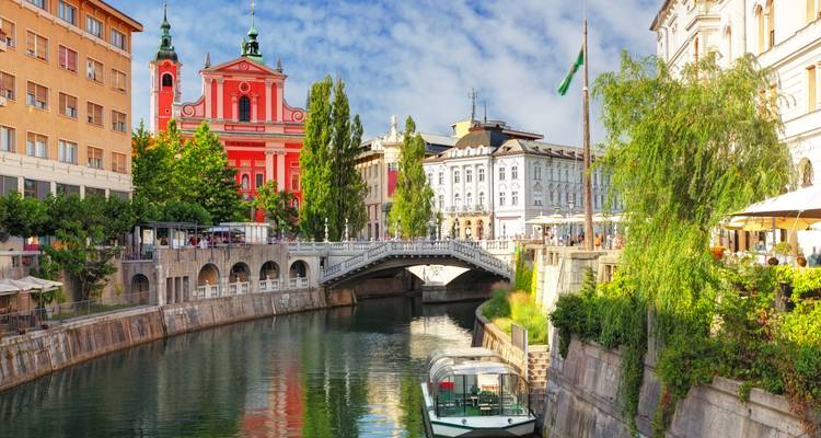 The vibrant pink Franciscan Church and Triple Bridge spanning the Ljubljanica River framed by historic facades and greenery.