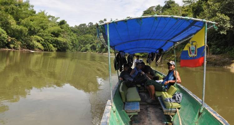 Kleine gemotoriseerde kano met reizigers die een rustige rivier in de jungle navigeren onder een blauwe bladerdak, Ecuadoraanse vlag aan de achterkant.