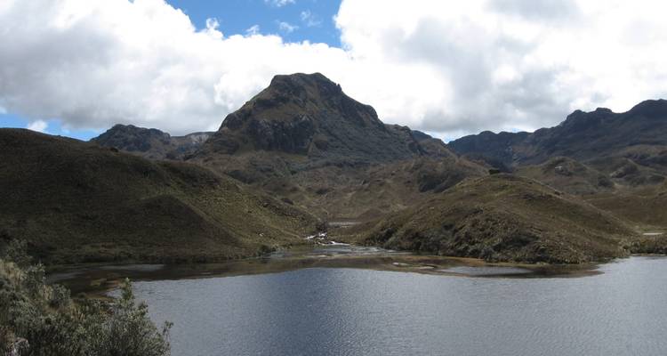 Un lago de gran altitud refleja un pico escarpado rodeado de pastizales de páramo ondulante en el Parque Nacional El Cajas.