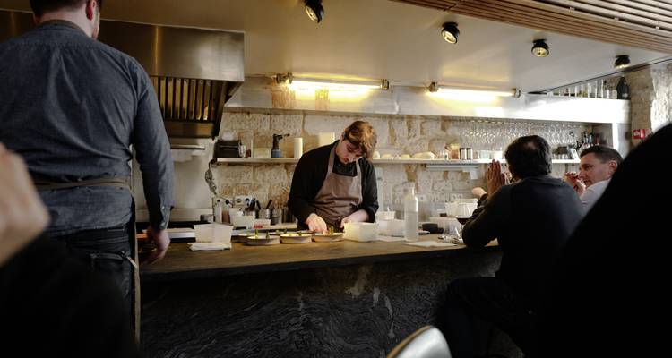 Open keuken bistro waar een chef gerechten bereidt terwijl gasten aan de bar zitten.