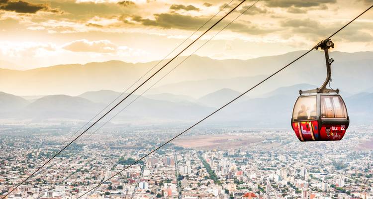 Téléphérique coloré glissant haut au-dessus de la ligne d'horizon de Salta avec les montagnes andines brumeuses en arrière-plan.