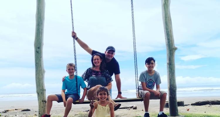 Familia posando en un gran columpio de madera en una playa tropical