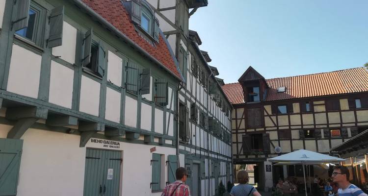 Narrow courtyard lined with half-timbered historic buildings, small art gallery sign and visitors strolling under blue sky.