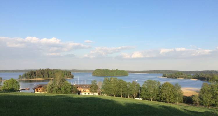 Peaceful lake dotted with wooded islets and a small marina viewed from a green meadow under a clear evening sky.