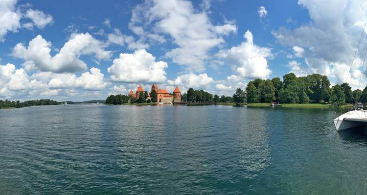 Wide lake panorama with Trakai Castle’s red towers rising on an island beneath dramatic cumulus clouds.