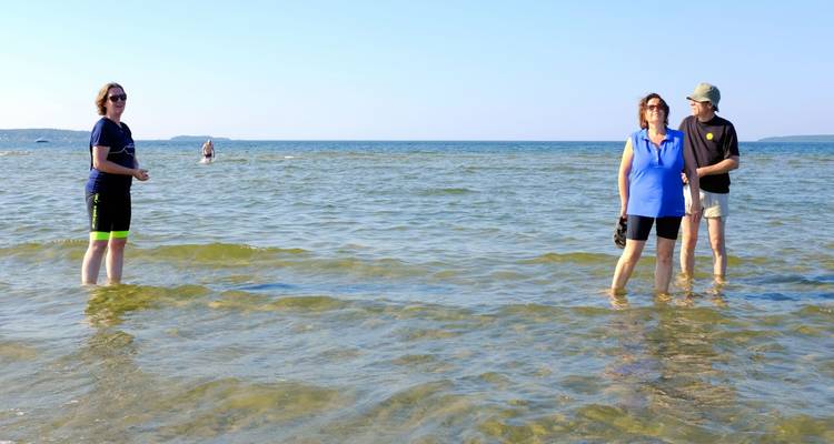 Travelers wade barefoot in shallow Baltic Sea water smiling in bright afternoon light.