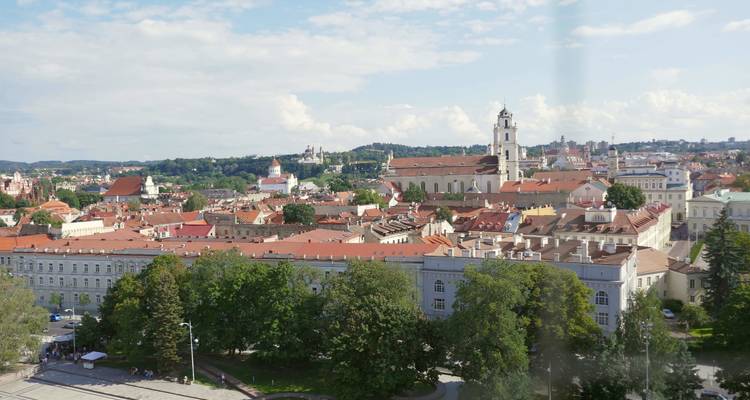 Elevated panoramic view of Vilnius Old Town’s red rooftops, church spires and green parks on a bright day.