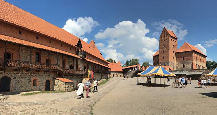 Inside Trakai Castle courtyard with striped medieval tents, visitors and stone walls under blue sky.