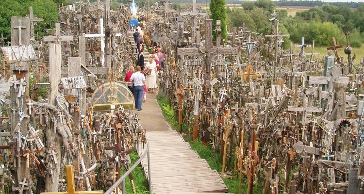 Wooden crosses crowd the famous Hill of Crosses pilgrimage site with visitors walking a narrow boardwalk.
