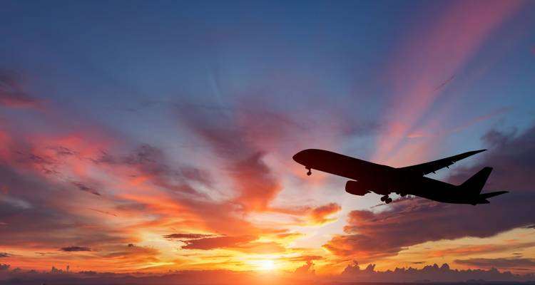 Silhouette of commercial airplane ascending against vivid multicolored sunset sky.