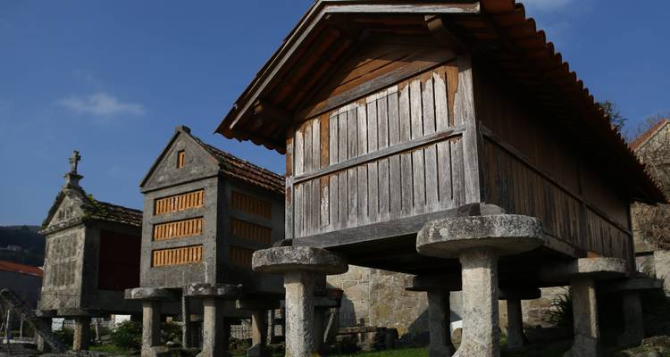 Traditional Galician stone granaries on raised pillars under clear blue sky.
