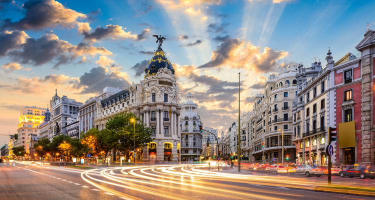 Gran Vía in Madrid at dusk, featuring the Metropolis Building under a dramatic sky with light-trail traffic.