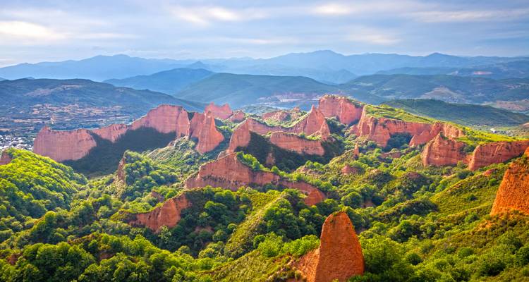 The red, jagged cliffs and green forests of Las Médulas contrasted against distant mountains.