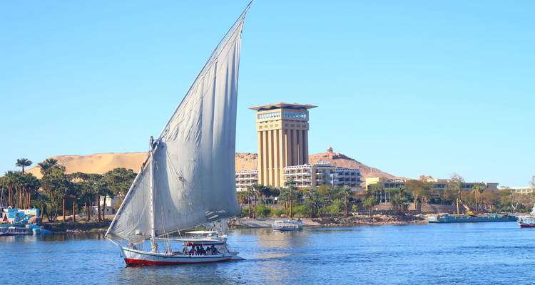 Une felouque classique toutes voiles dehors glisse le long du Nil devant les bâtiments riverains modernes d'Assouan.