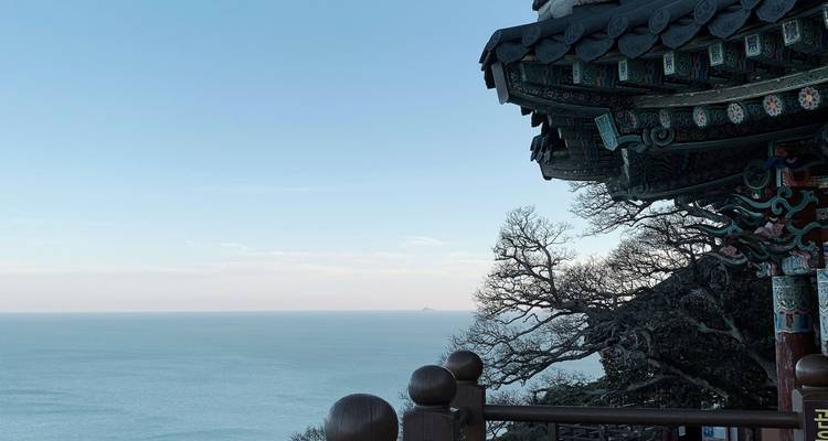 Decorative wooden eaves of a seaside temple overlook a calm blue ocean and distant horizon.