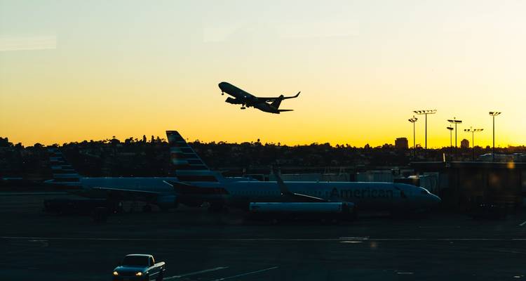 Silhouette eines startenden Flugzeugs über geparkten Jets auf der Landebahn bei Sonnenaufgang
