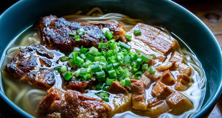 Nahaufnahme einer reichhaltigen Schweinefleisch-Nudelsuppe, garniert mit gehackten Frühlingszwiebeln