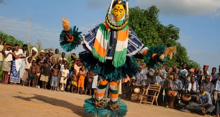 Bailarín disfrazado colorido realizando un energético baile tradicional con máscara ante una multitud en un pueblo rural